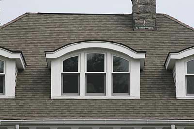 Bílé vikýře ve tvaru obočí na vrcholu zakřivené hnědé střechy.
