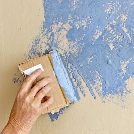 Person bruger pap til at give maling et struktureret look på væggen