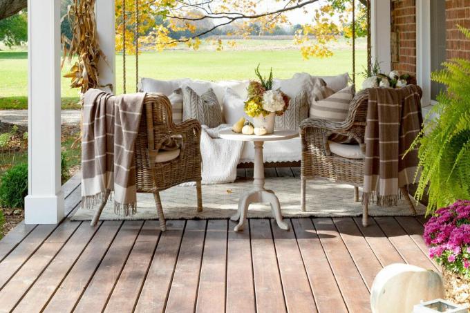 Un porche delantero con un gran columpio, dos sillas de mimbre y mucha decoración acogedora y cálida. 