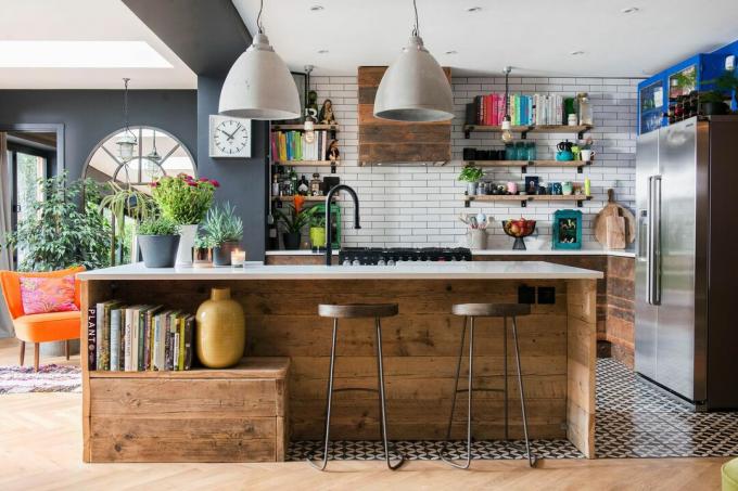 Een moderne keuken met rustieke houtaccenten. Boeken worden opgeborgen op het keukeneiland en op open planken, waardoor de kamer een vleugje kleur krijgt. 