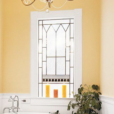 Okno do koupelny se zlatými detaily a svíčkami na malém parapetu.