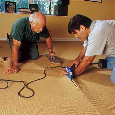 Vyrai sujungia kilimą naudodami elektrinę siuvimo geležį, siūlę ir svorį