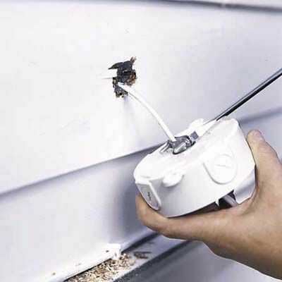Man fäster en rund utloppslåda för att installera utomhusstrålkastare i garage