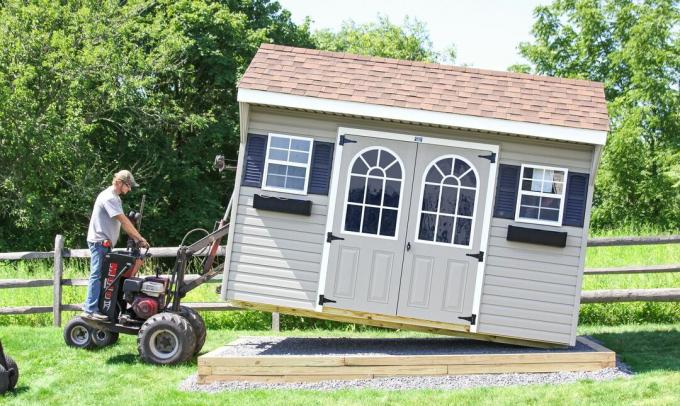 Člověk používá vysokozdvižný vozík k umístění montované zahradní kůlny na pozemek