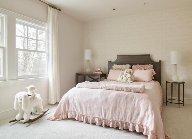 Malá ložnice s jednobarevným světle růžovým barevným schématem. Na podlaze a na posteli ležely bílé hračky. 