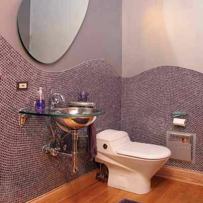 Två tonat lila badrum med små fyrkantiga plattor på väggarna och en oval formad spegel. 