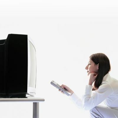 Person som sitter framför en gammal lådformad tv som håller en fjärrkontroll.