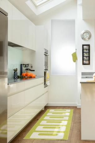 Una cocina de galera minimalista con gabinetes blancos y una alfombra verde brillante. 