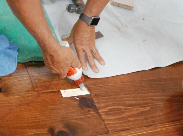 Muž lepí drevenú záplatu na štiepanú podlahu