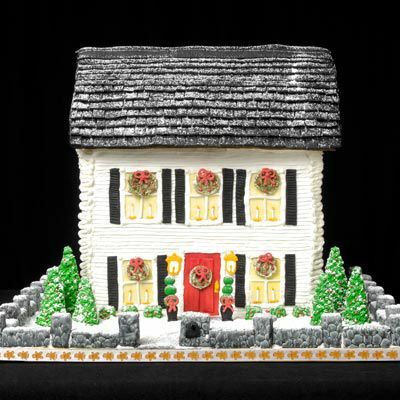 Lebkuchenhaus mit weißer Zuckerglasur außen und Fenstern mit Kränzen und schwarzen Fensterläden. 