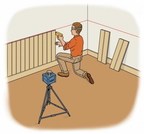 Osoba montująca boazerię na ścianie i używająca poziomicy laserowej do oznaczenia wysokości.