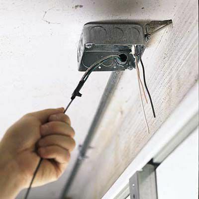 Čovjek povlači žice kroz cijev kako bi instalirao vanjska garažna svjetla