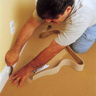 Mannen bruker teppebeisel for å tvinge teppekanten inn i rommet under gulvlisten