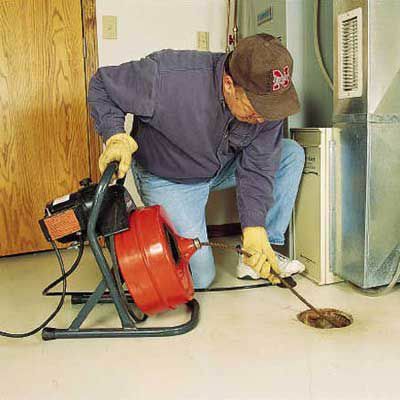 Person som använder en kraftskruv för att rensa ett golvbrunn.