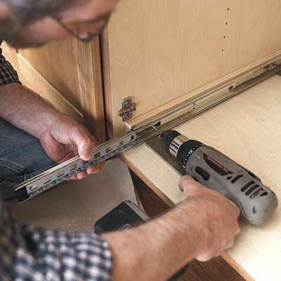 Muž montuje sklíčka vytahovacích polic do kuchyňských skříněk