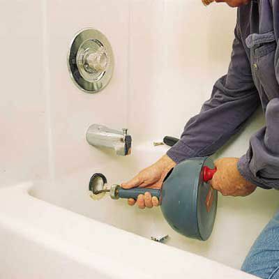 Person som skär igenom en täppa i ett badkar med en kabel, även känd som rörmokarens orm.
