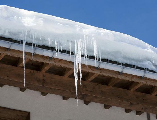 Polei lungi și zăpadă deasupra acoperișului și jgheabului unei clădiri.