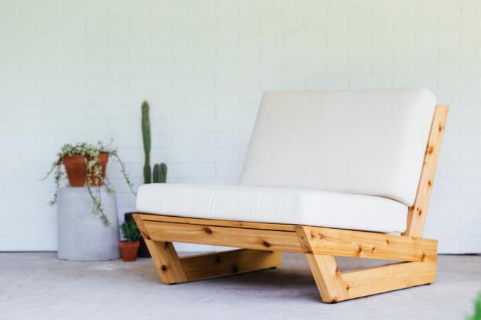 Μια μοντέρνα ξύλινη πολυθρόνα με λευκά μαξιλάρια. 