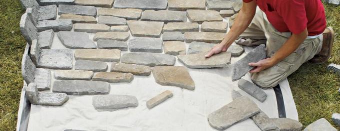 Person, die viele verschiedene Steine ​​auf dem Boden auslegt, um sich auf den DIY-Steinkamin vorzubereiten.