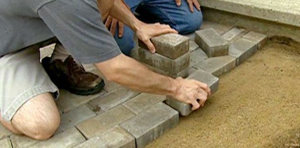 Oameni care așează cărămizi pentru a construi o pasarelă de pavaj.