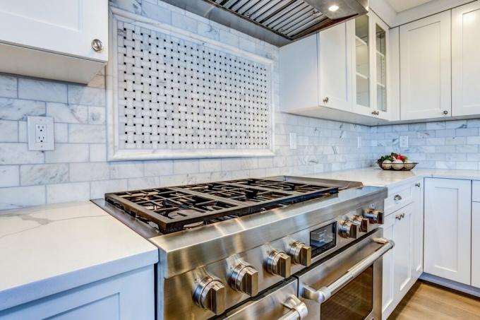 Hvitt kjøkken med hette i rustfritt stål over gasskomfyr. 