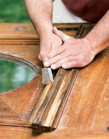 El hombre usa pequeños raspadores para raspar las molduras de la puerta de madera