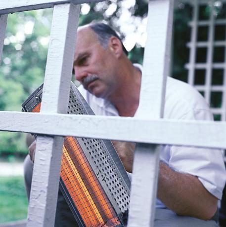 Omul folosește un instrument de încălzire cu infraroșu pentru a îndepărta vopseaua veche de pe casă 