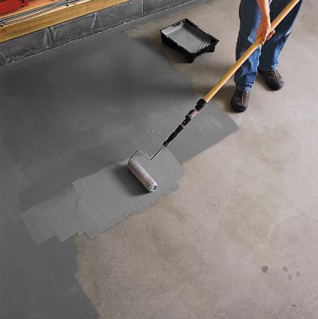 Persoon die een roller gebruikt om epoxyverf op de garagevloer aan te brengen.