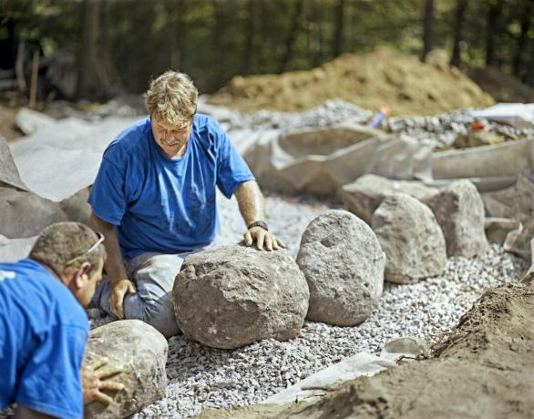 גברים מניחים קורס ראשון של אבנים של קיר אבן עצמאי
