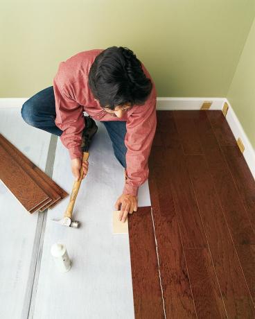 Man installeert resterende zwevende houten vloerplanken 