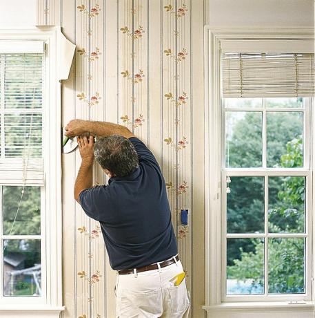 Hombre recortando papel tapiz alrededor de ventanas y puertas